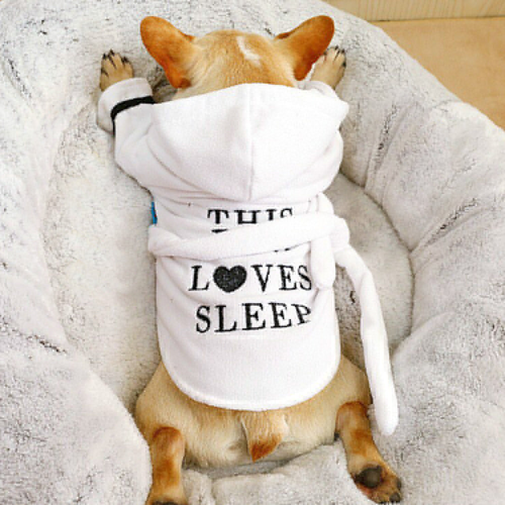 White Hooded Dog Bathrobe – dog wearing a white robe with text, lying on a fluffy surface